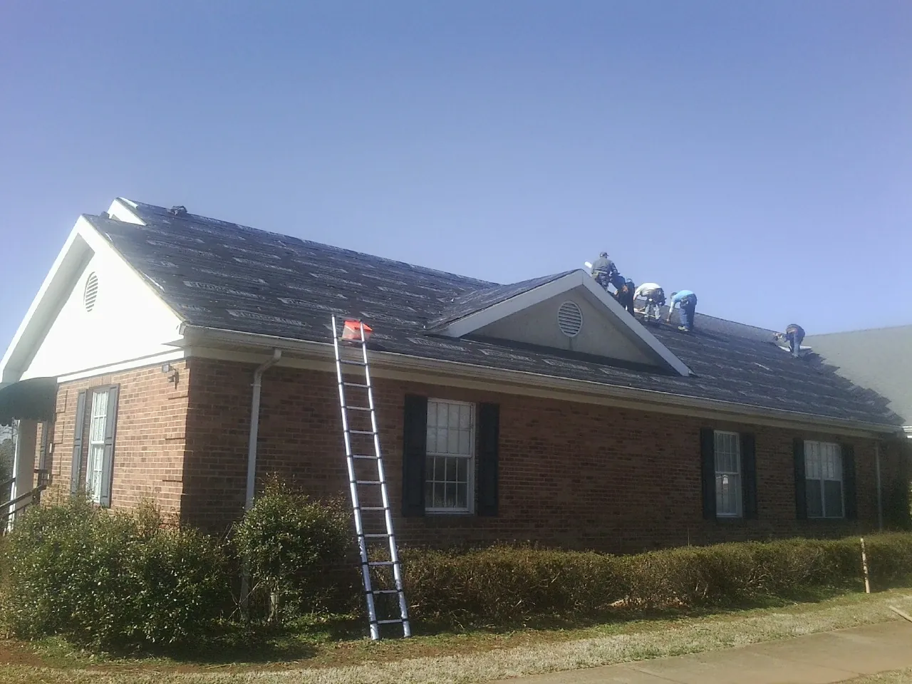 Crew tearing shingles off a brick ranch roof with a ladder set — Emergency Roof Repair work by our crew in Panama