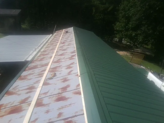 Old rusted panels beside newly installed green metal roofing — Wind Damage Roof Repair by Roofing Brothers in Panama