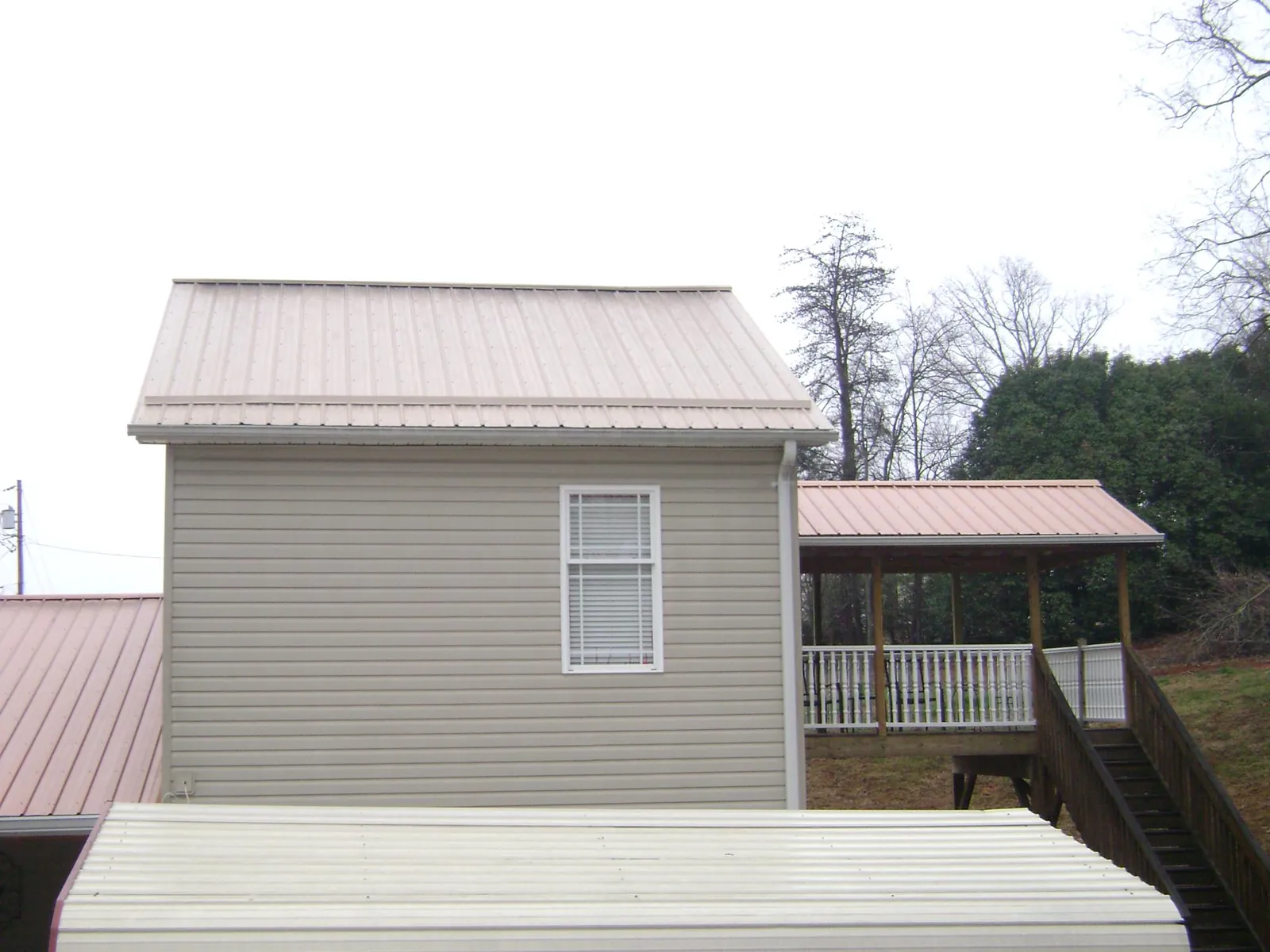Tan metal roofs on a two story addition and attached porch, from a Roof Replacement job in Panama